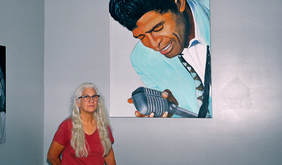 Artist Jo Jensen stands next to her painting of musician James Brown, which hangs in the Ideal Bar.