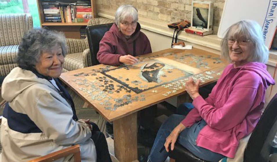 Older adults work on a jigsaw puzzle in the Goodman Community Center senior lounge.