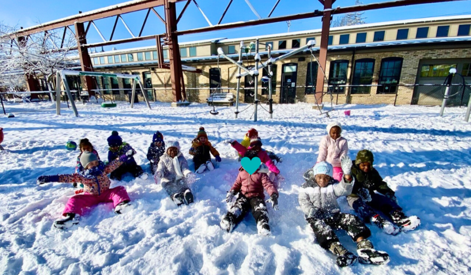 A group of preschool kids play in the snow on a sunny day at the Goodman Community Center.