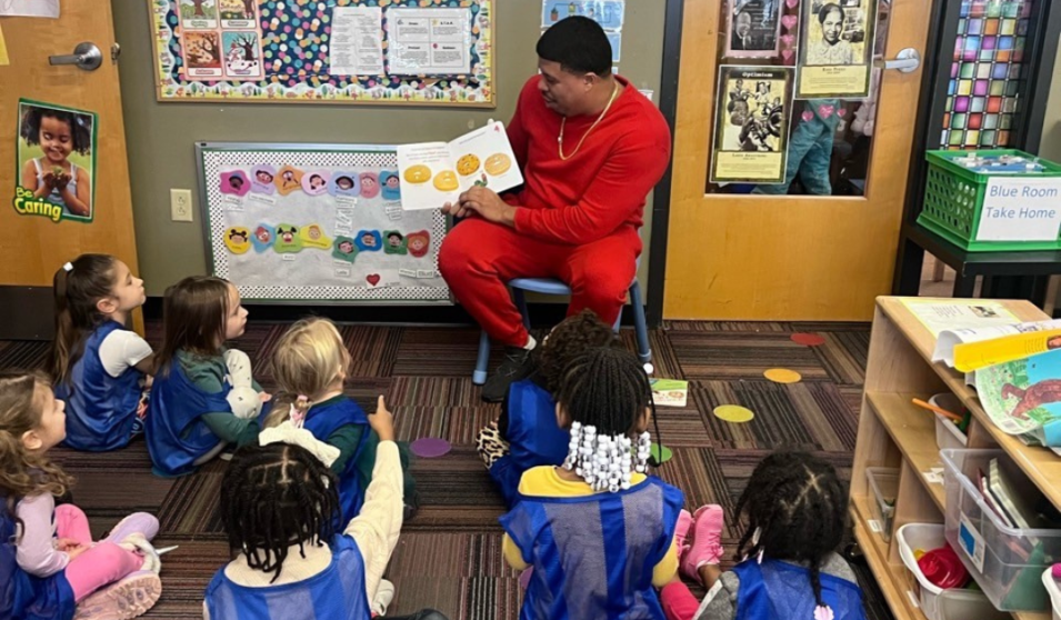 A father reads a book to his daughter's 4K class at the Goodman Community Center