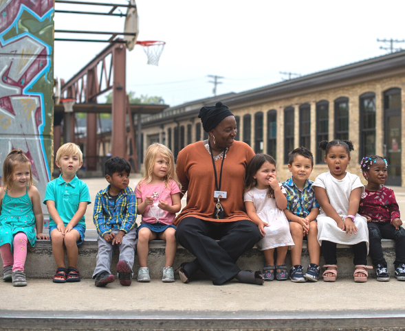 Goodman Center CEO Letesha Nelson sits in a line with a group of preschool students.