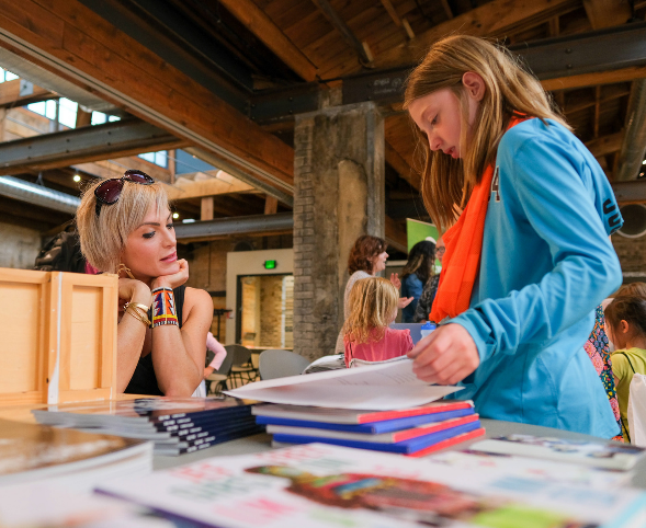 A professional woman looks on as a young girl pages through information at a Girls Inc. career fair.