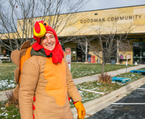 A person dressed as a turkey smiles in front the Goodman Community Center.