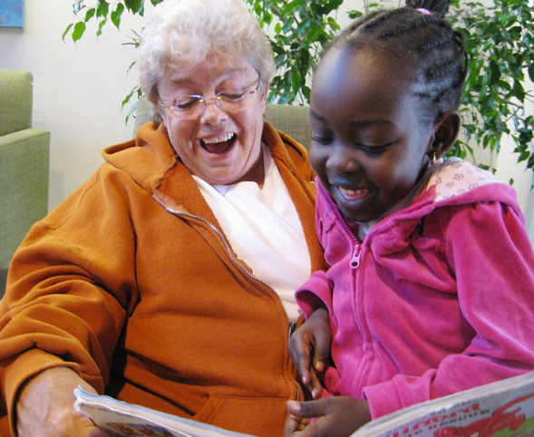 An older woman reads a book to a young girl