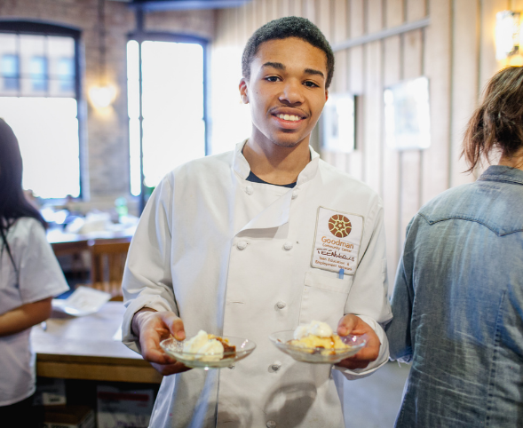 A teen holds two plates of food he helped prepare for a Cajun dinner at the Goodman Center.