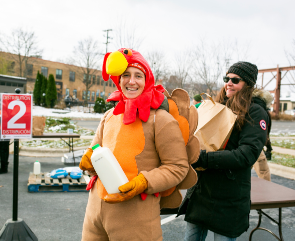A person dressed in a turkey costume smiles with a half gallon of milk while distributing groceries at Goodman's Thanksgiving Basket Drive.