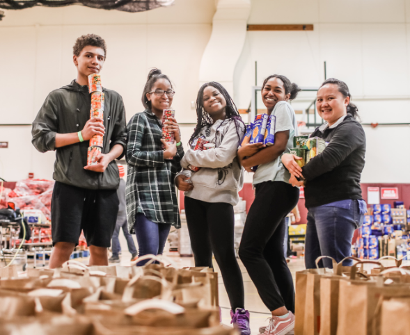 Five volunteers hold food at the Goodman Community Center Thanksgiving Basket Drive.