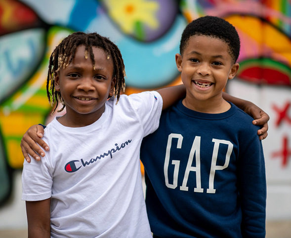 Two boys with their arms around each other in front of a graffiti wall