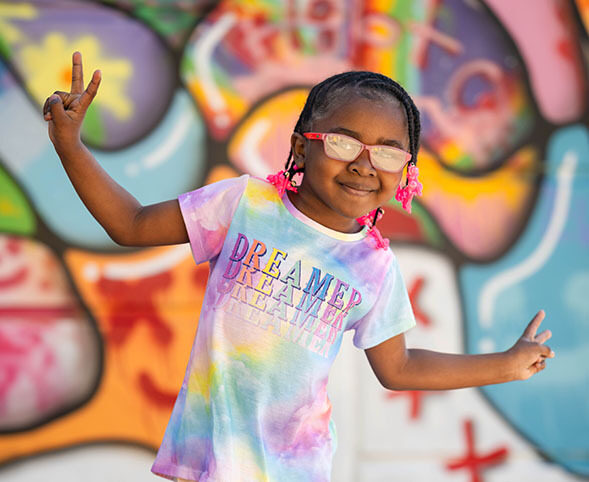Colorful portrait of a young girl wearing tie dye giving peace signs in front of a graffiti wall
