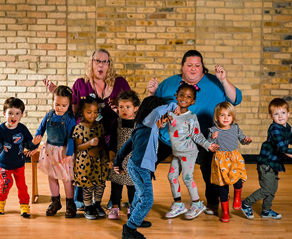 Two teachers with a group of preschool students dancing and being silly.
