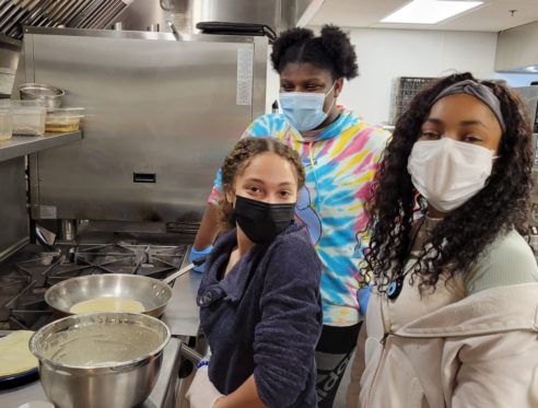 Three students work in an industrial kitchen making beignets.