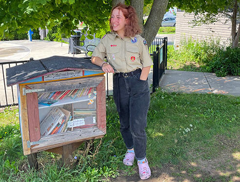 Naomi Wetzel, a Scout from Troop 747, leans on the Goodman Community Center's Little Free Library.