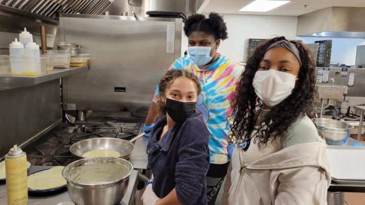 Three students stand over a mixing bowl and frying pan as they work to make beignets.