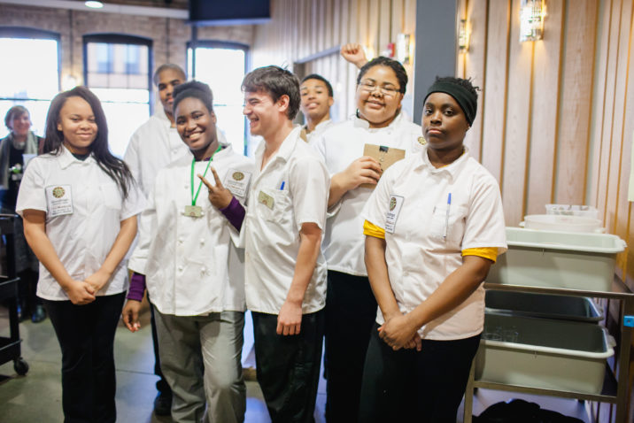 A group of teens in chef coats posing for a picture