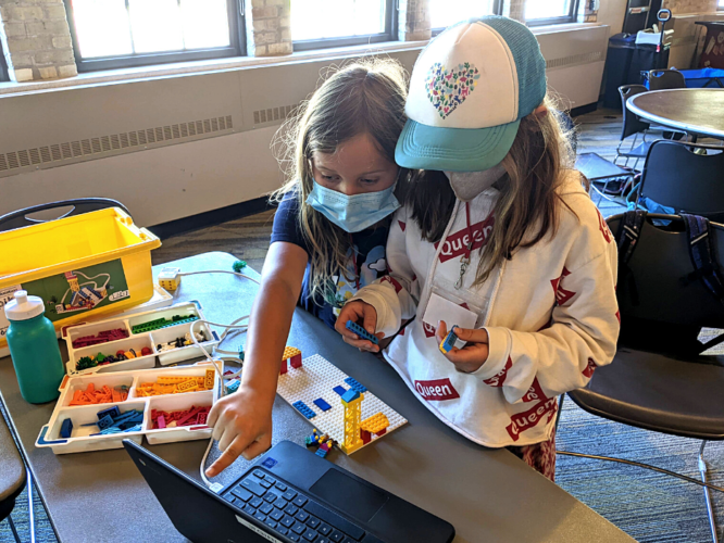 Two girls build a structure with Legos that are linked to a computer program.