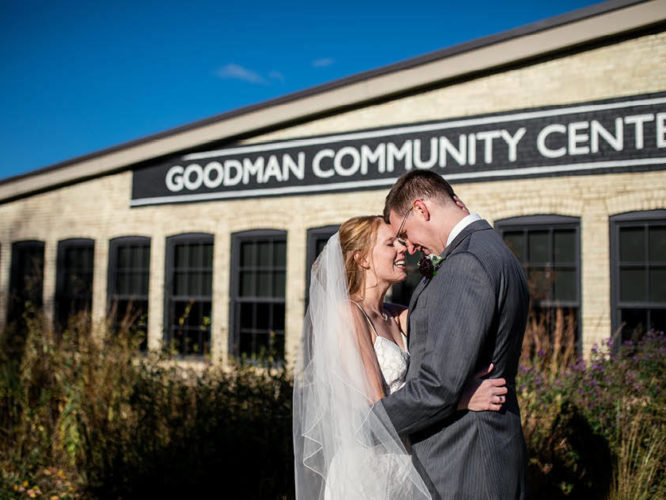 A bride and groom posing in front of the Goodman Community Center