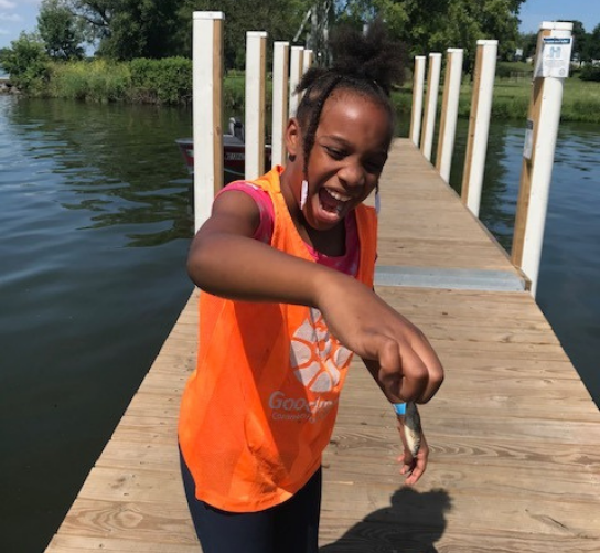 An African American girl laughs while holding a very small fish she caught.
