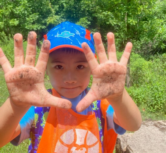 A young Asian boy holds up his hands to show the dirt from playing and exploring.