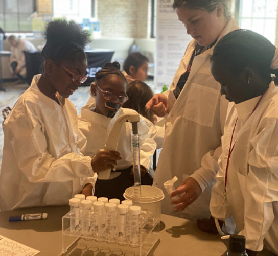 A group of girls in white lab coats are doing an experiment with test tubes and other scientific equipment.