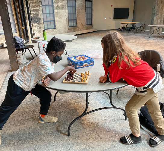 Two students lean on a table as they play a game of chess.