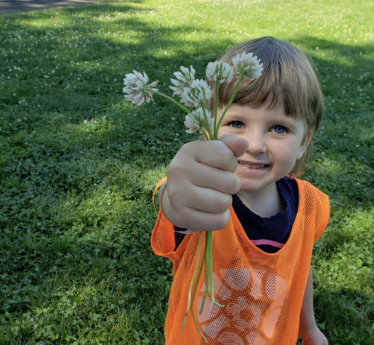 A child stands outside and holds up a handful of clovers.