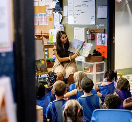 A preschool teacher reads a book to a classroom of students.