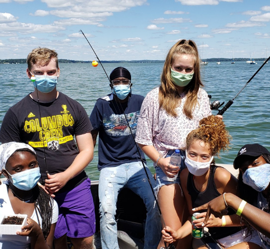 Students hold fishing poles on a boat.
