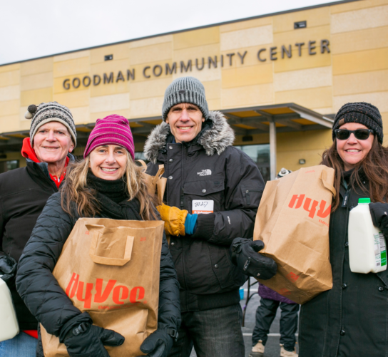 A group of volunteers hold grocery bags at the Goodman Center Thanksgiving Basket Drive.