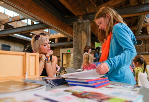 A professional woman looks on as a young girl pages through materials at a Girls Inc. career fair.