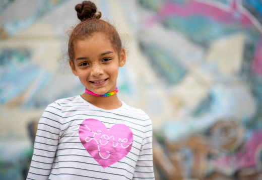 A young girl wearing a heart t-shirt smiles at the camera.