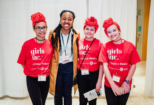 Three girls wearing Girls Inc. shirts and read head wraps pose smiling for the camera.