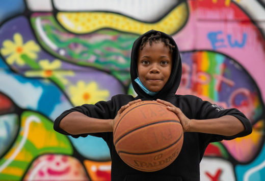 Young boy with basketball standing in front of graffiti wall