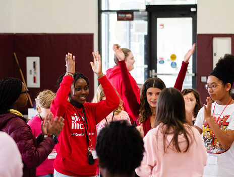 A group of girls with their hands up, clapping together for an activity.