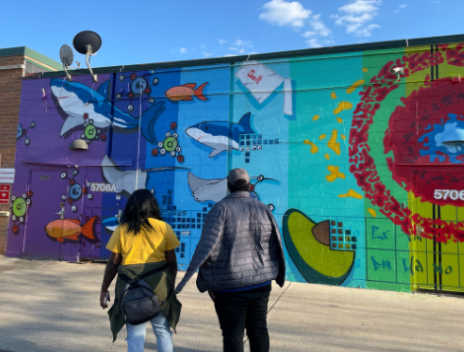 Two teens stand with their backs to the camera in front of a brightly colored mural.