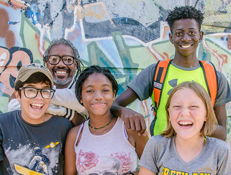 Smiling middle schoolers and a teacher in front of a graffiti wall