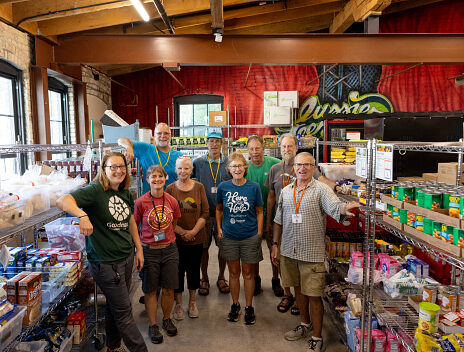 Food pantry team stand with volunteers in the center of Goodman's food pantry.