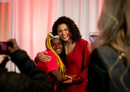 A mixed race woman hugs a young Black girl at a gala celebrating Girls Inc. of Greater Madison.