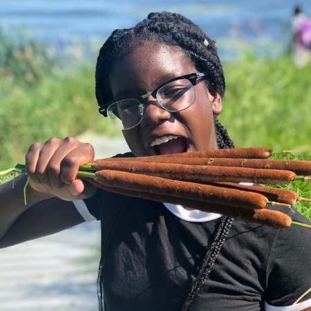 A student holds a handful of cattail plants, pretending to eat them, at Cherokee Marsh.