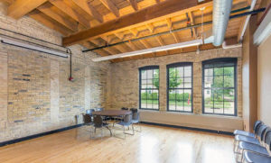 An empty sunny room with polished wood floors and exposed brick