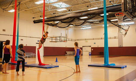 Women in gymnasium hanging from ceiling on aerial silks