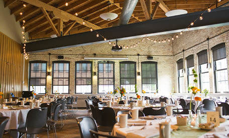 A beautiful industrial room decorated for a wedding reception with string lights and flowers